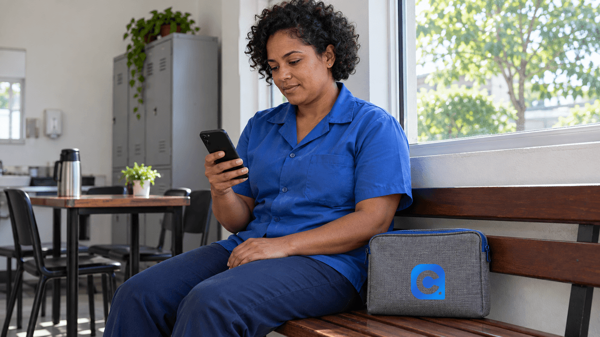 Trabalhadora de camisa azul consulta celular no intervalo, com símbolo Meu Consig na nécessaire cinza ao lado.