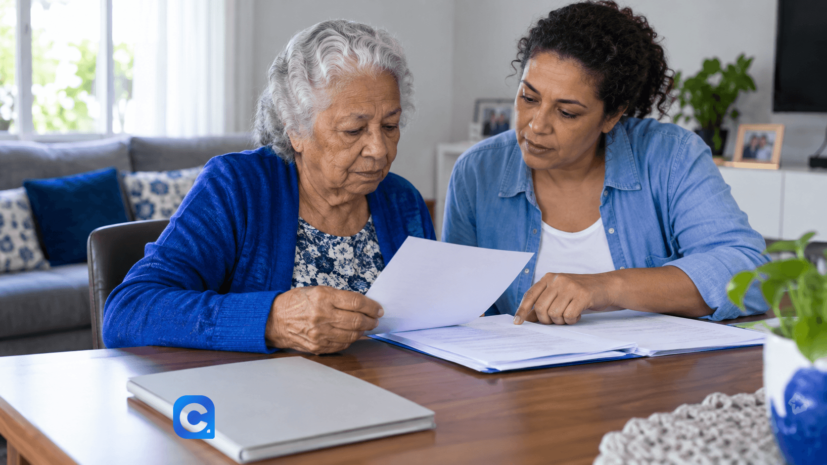 Mulher idosa e familiar leem documentos juntas em casa.